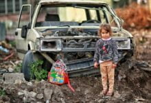 girl with backpack near broken car ruins